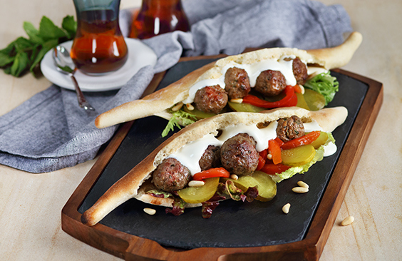 Samoon bread with cream cheese, kofta meatballs, fresh salad leaves, pickled cucumbers and pine nuts